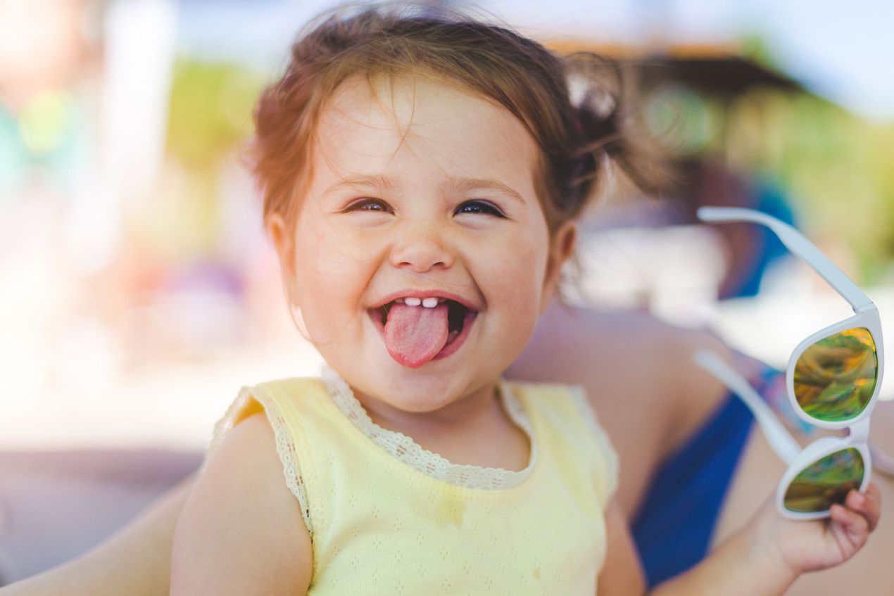 Smiling child in a yellow top holding white sunglasses outdoors