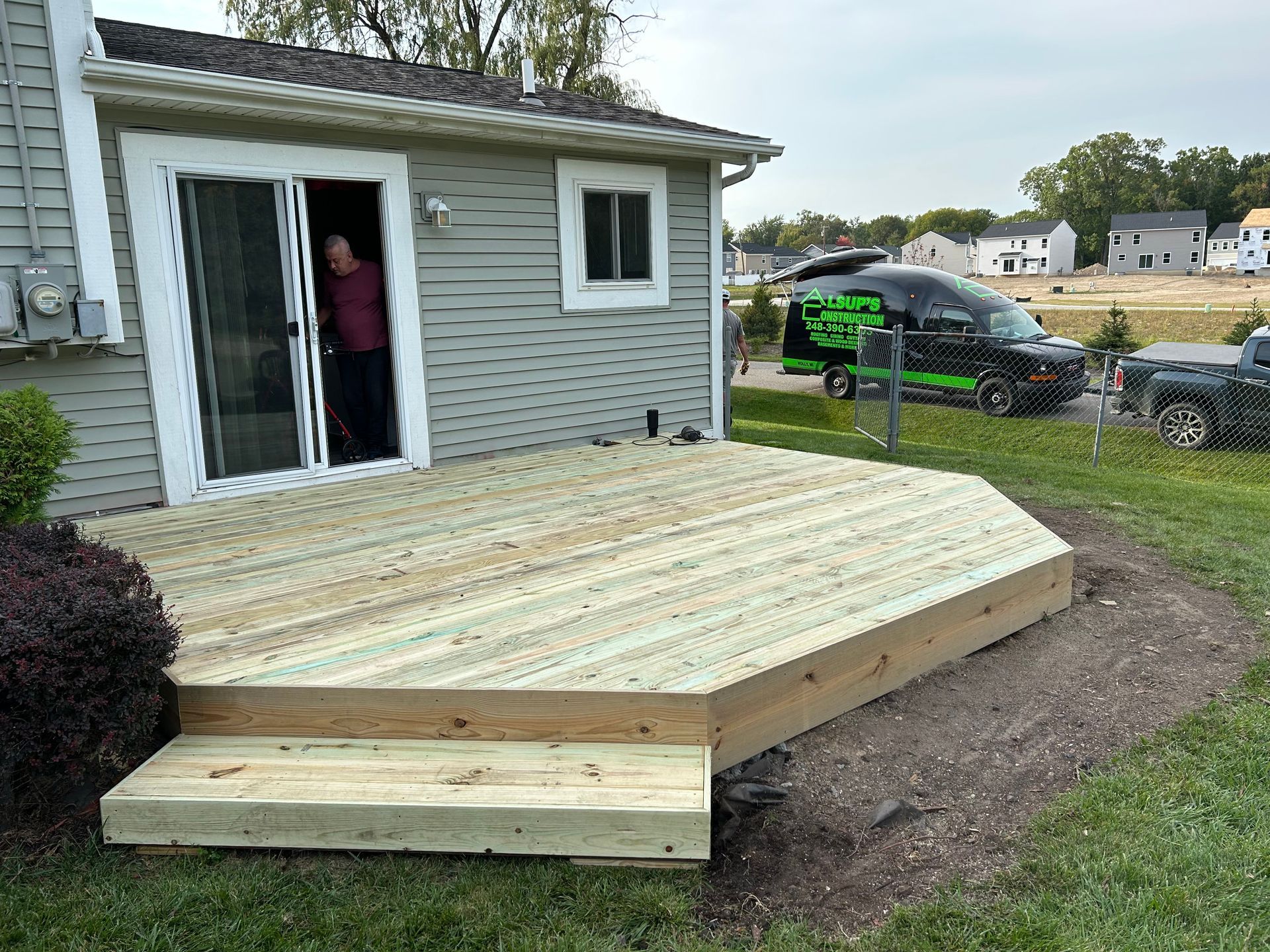 Wooden wheelchair ramp and deck beside a gray house, with a person standing in the doorway
