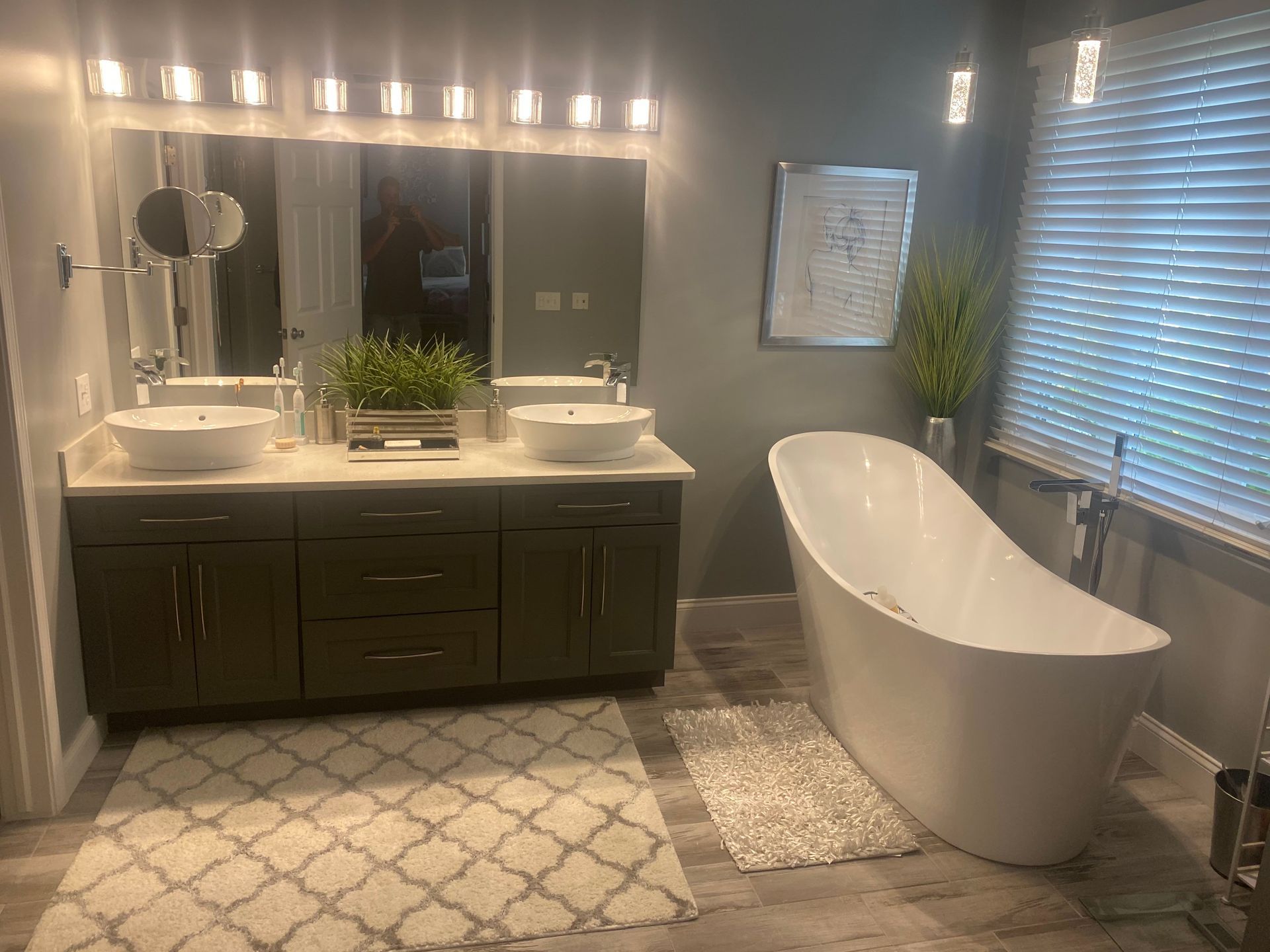 Modern bathroom with double vanity, freestanding tub, large mirror, and patterned rug.