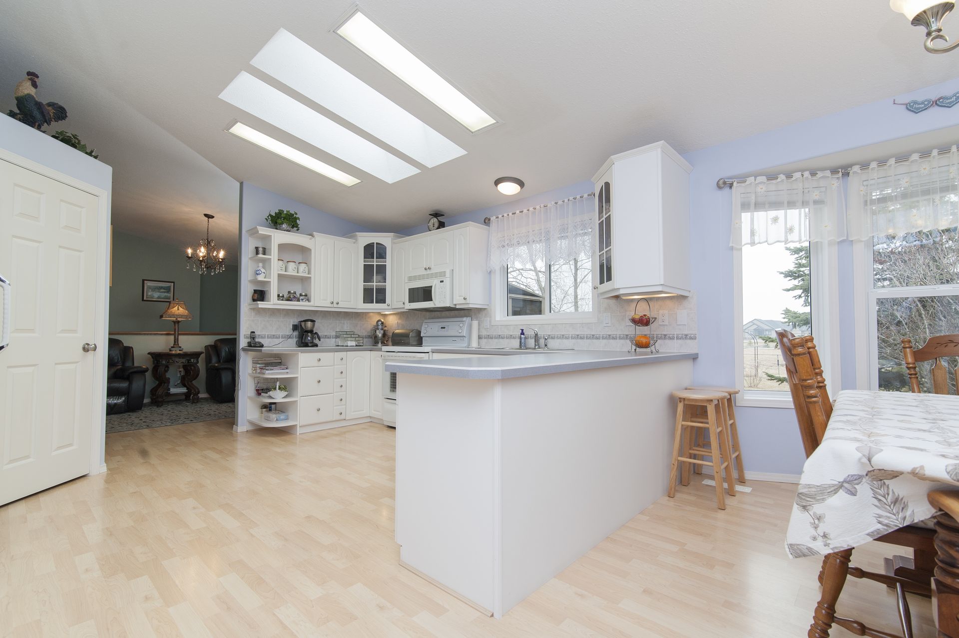 Bright white kitchen with skylights, island counter, large windows, and adjacent dining nook.