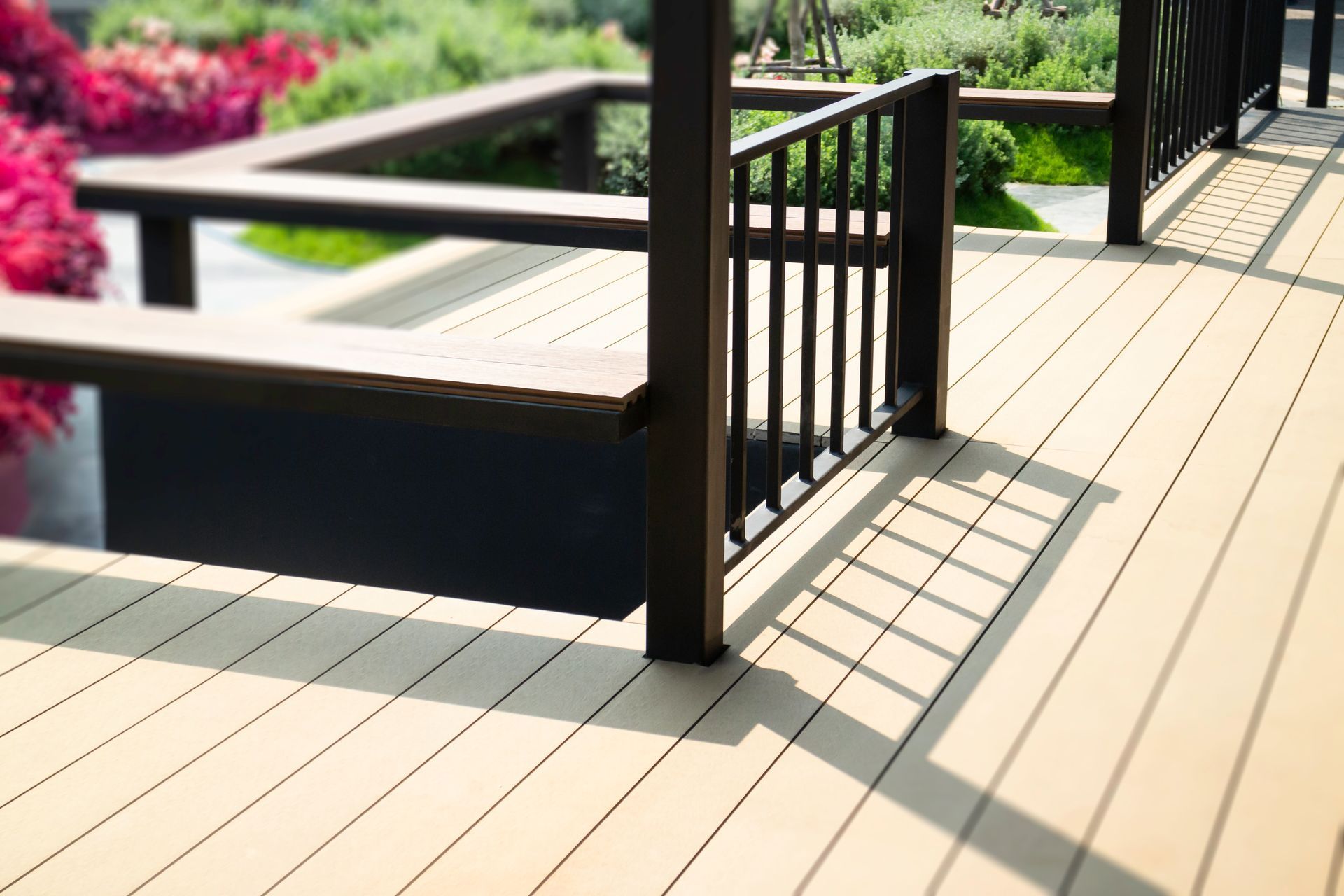 Sunlit beige deck with dark railings and posts, overlooking a landscaped garden.