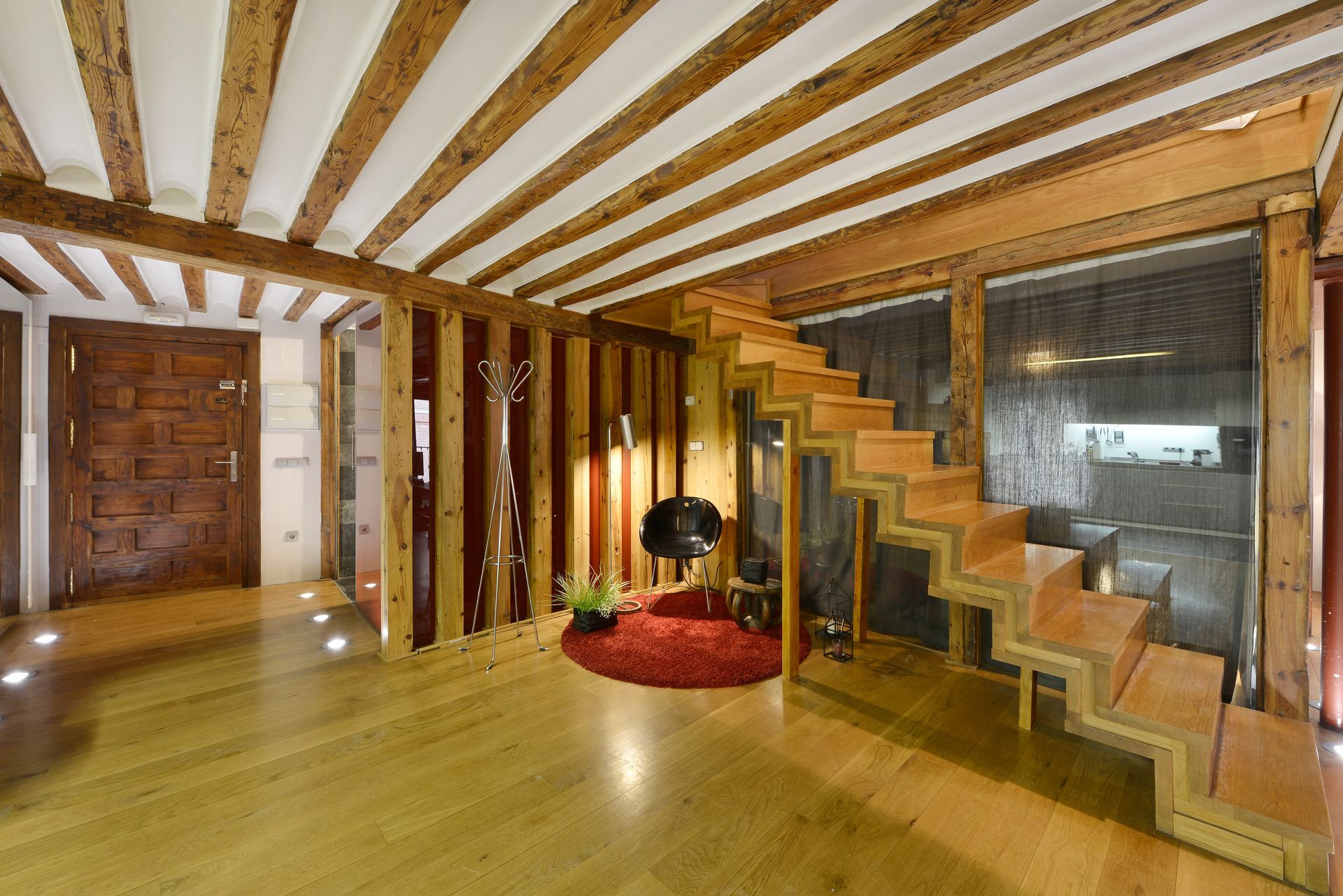 Warm wooden interior with exposed beams, floating stairs, and cozy seating nook.