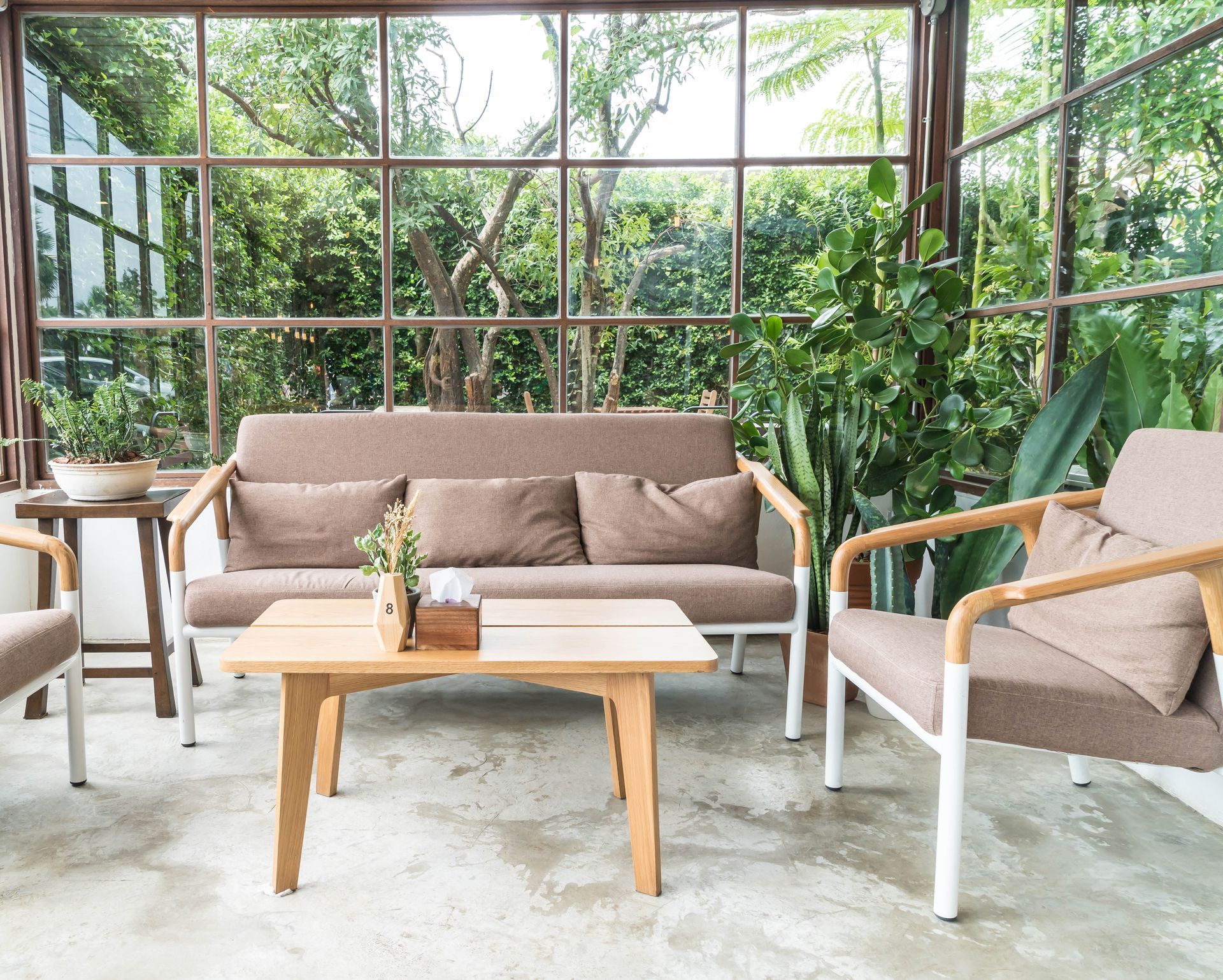 Sunlit indoor seating area with sofa, chairs, coffee table, and lush garden views.