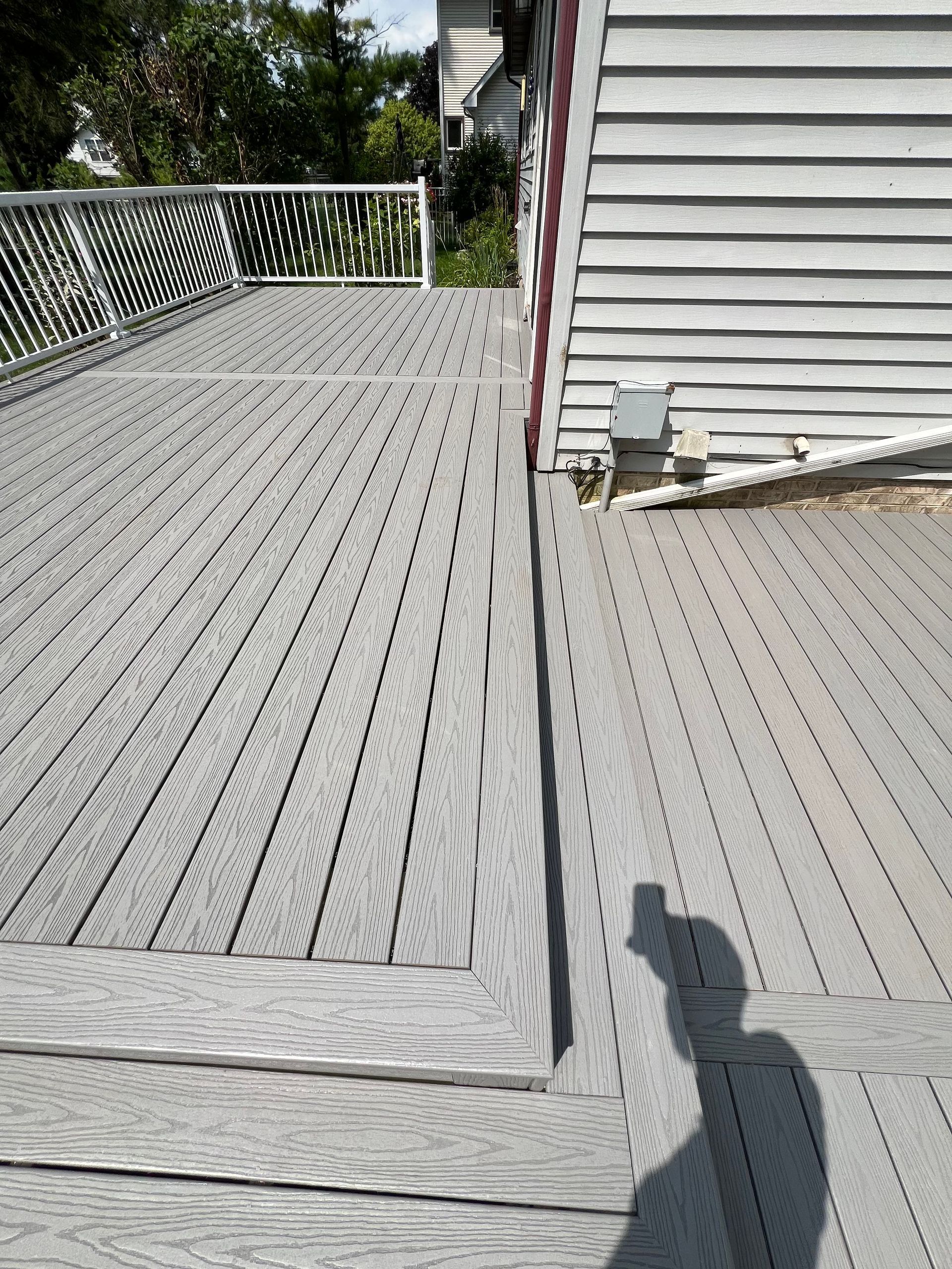 A shadow of a person is cast on a wooden deck next to a house.