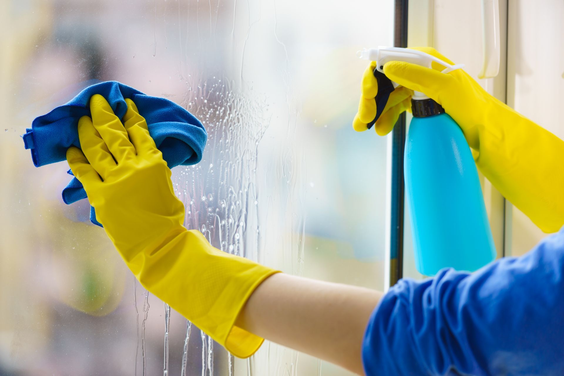 A cleaning professional wiping a glass window with spray and cloth.
