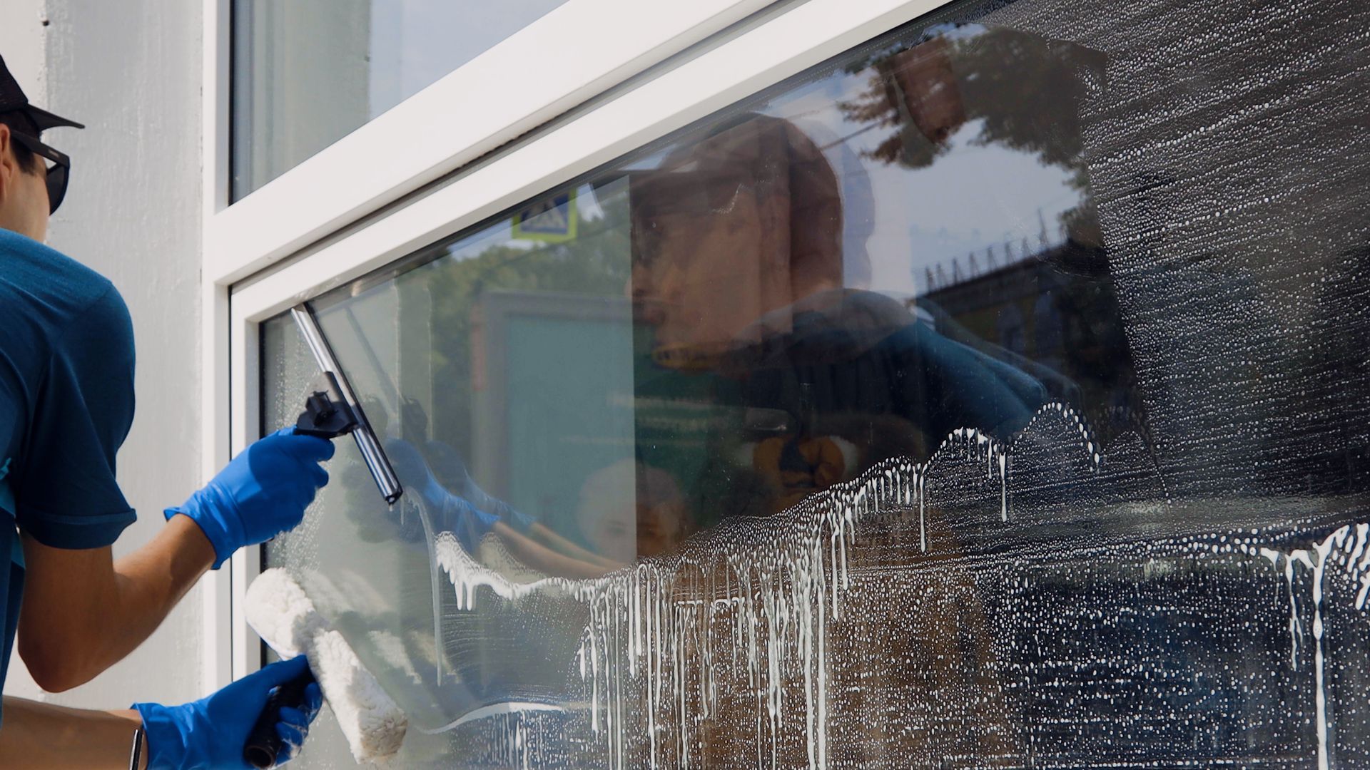 Close-up of a professional worker wearing blue gloves performing window cleaning service.