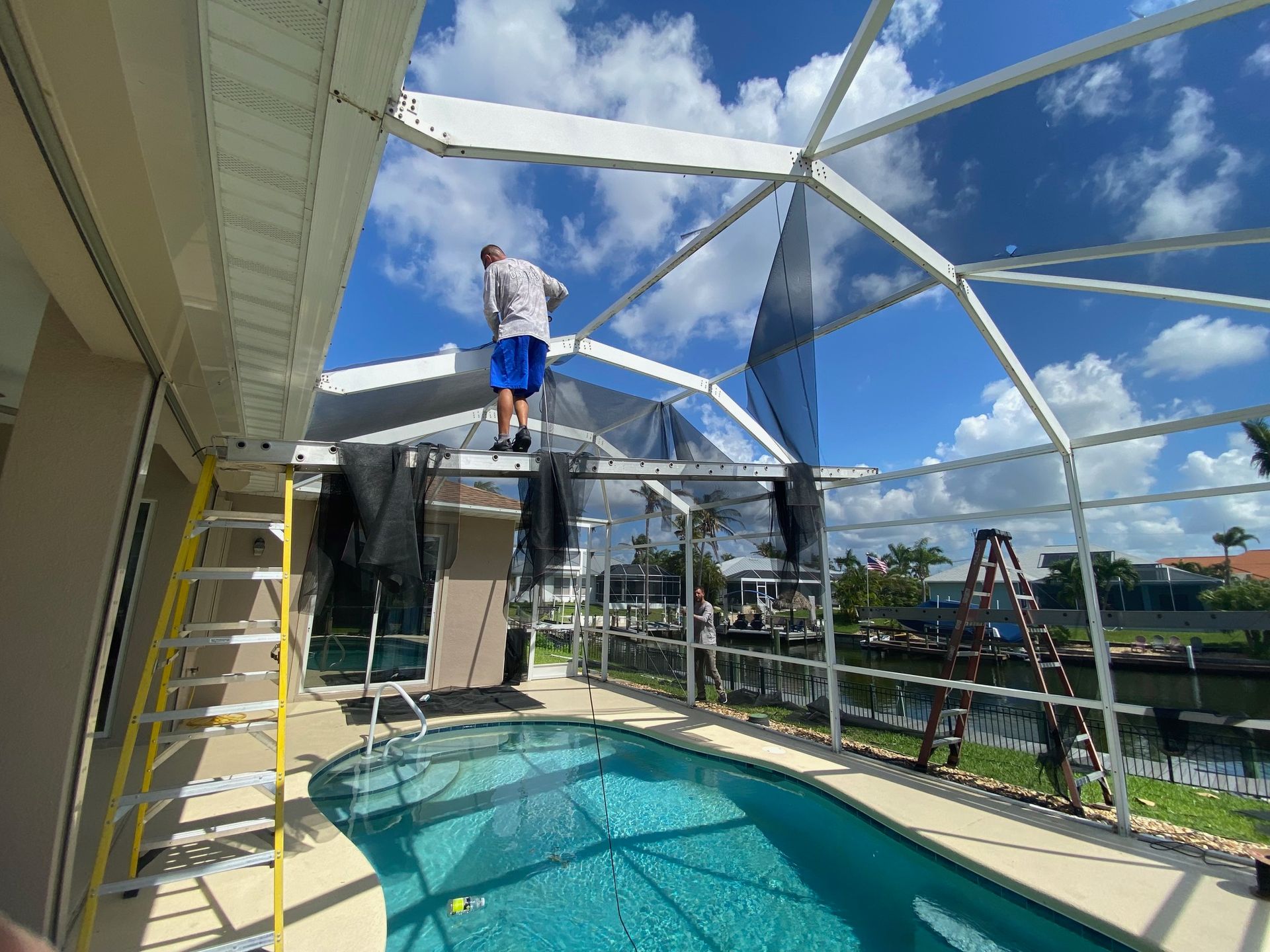 A man is standing on top of a ladder next to a pool.