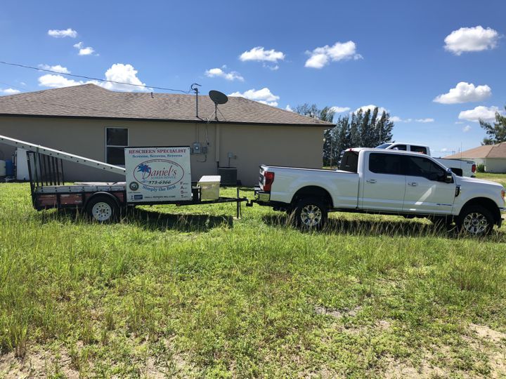 A white truck with a trailer attached to it is parked in a grassy field.