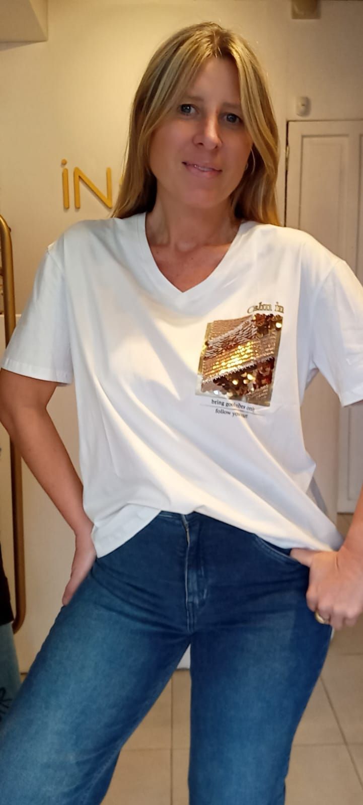 Mujer de pie en el interior de un edificio, con camiseta blanca y vaqueros azules, con las manos en las caderas.