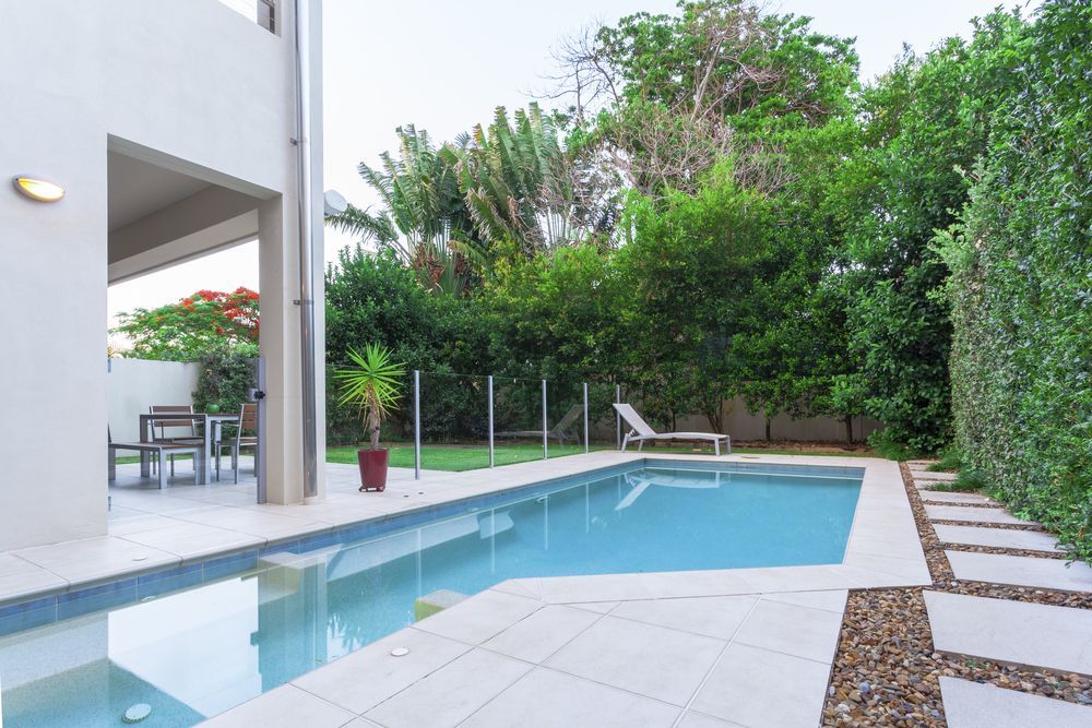Swimming pool in a backyard with patio furniture and lush green foliage — Tru Blu Pools & Spas in Bluewater, QLD