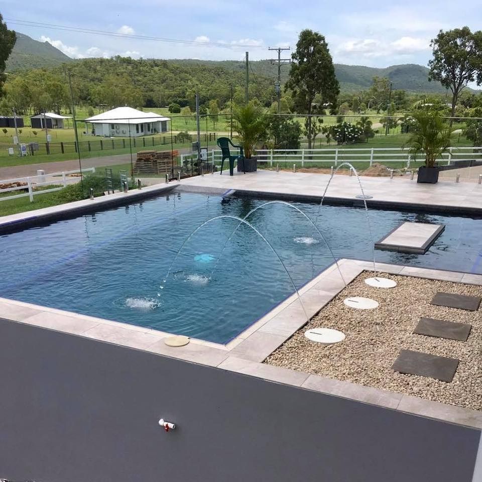 Swimming pool with water fountains, surrounded by stone and gravel patio, with a green landscape in the background— Tru Blu Pools & Spas in Bluewater, QLD