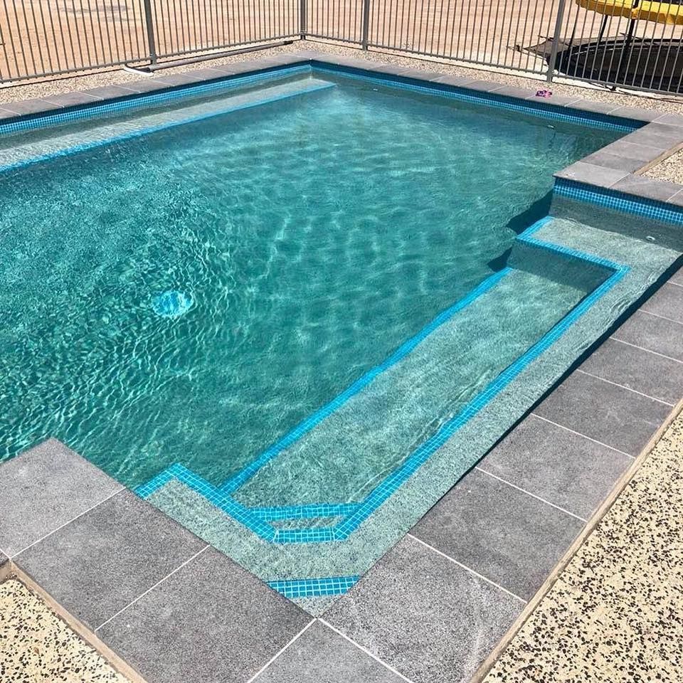 A rectangular swimming pool with blue water and tiled steps. Gray tiles surround the pool— Tru Blu Pools & Spas in Bluewater, QLD