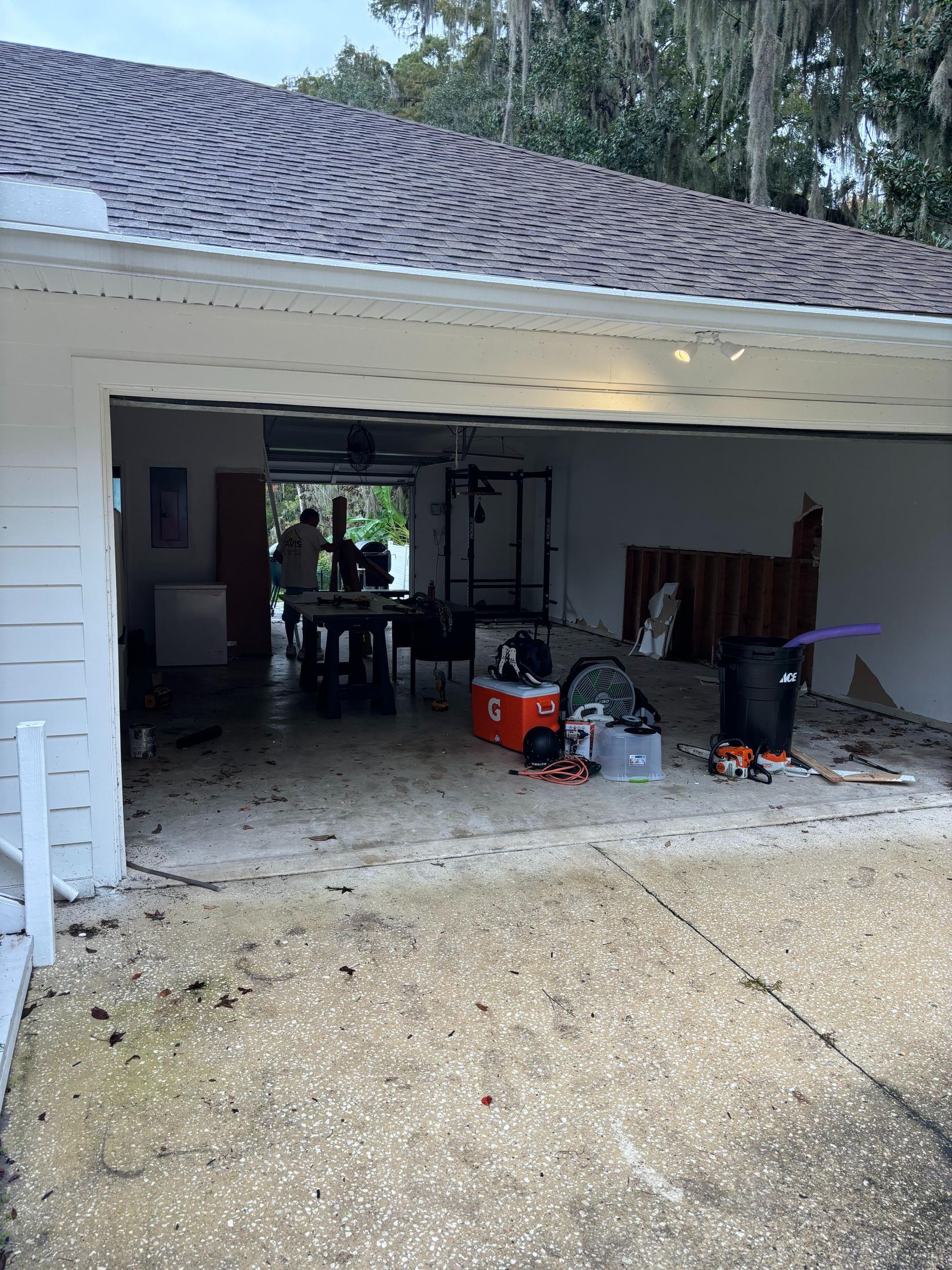Garage with debris, open door to living area with table and people. Overcast sky.