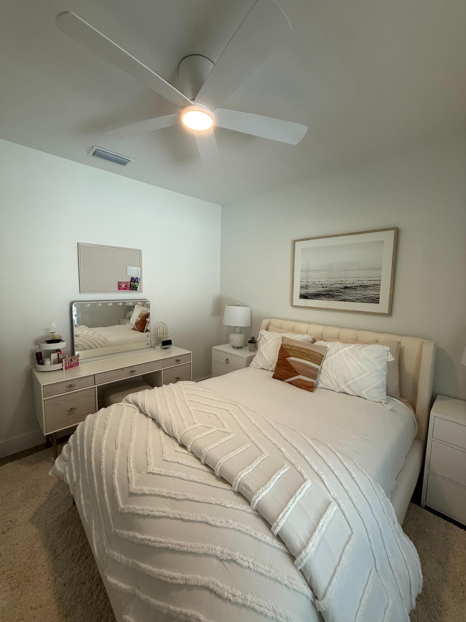 Bedroom with a bed, vanity, and a ceiling fan. Neutral colors with a white bedspread and walls.
