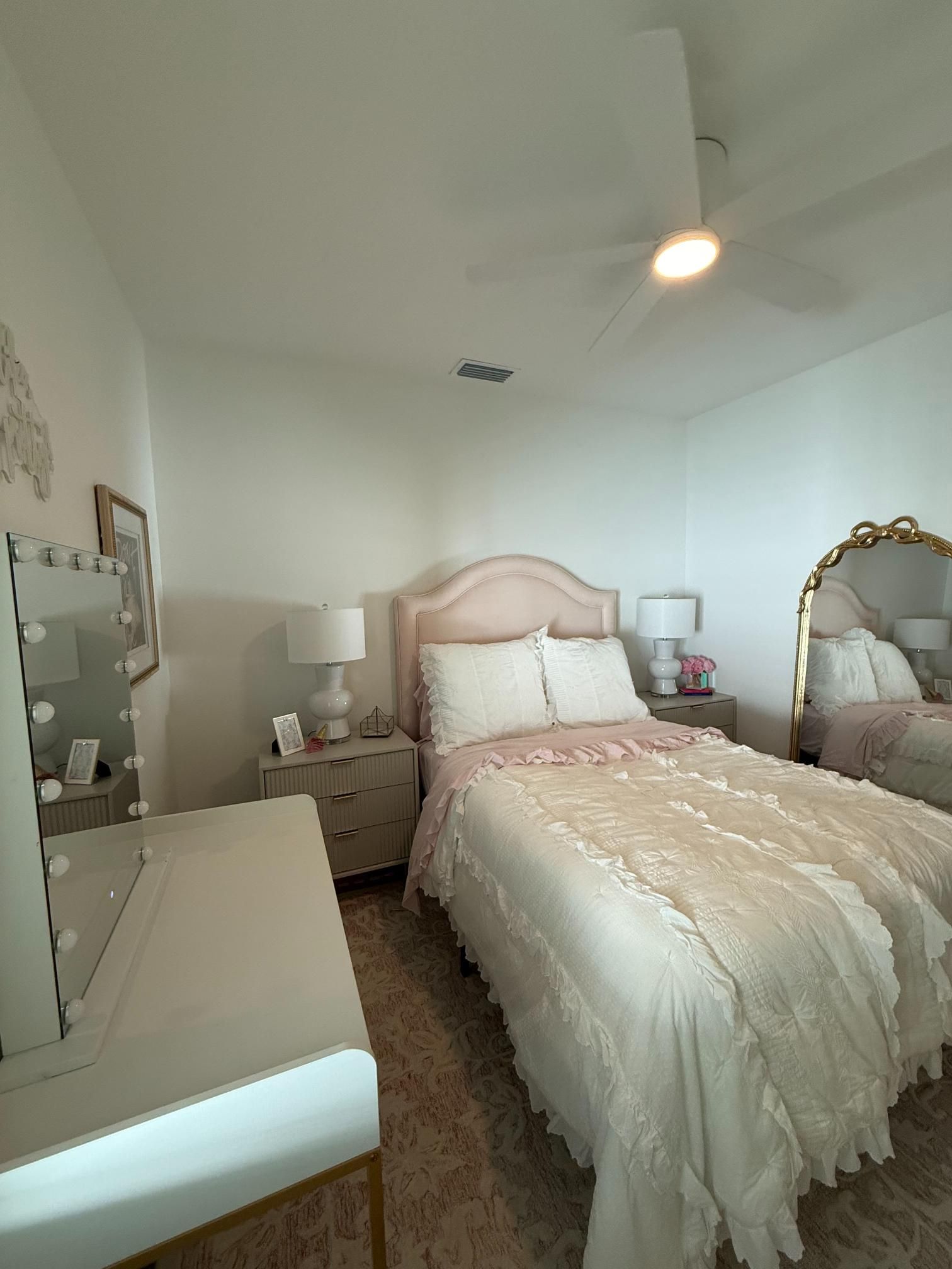 Bedroom with a bed, vanity, and large mirror, decorated in white and pink.