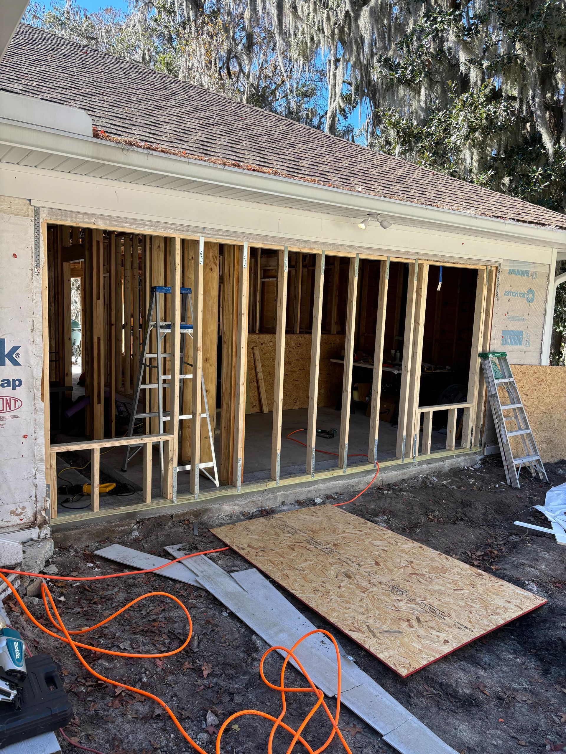 Garage under construction with exposed wooden framing and plywood on the ground.