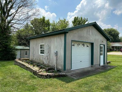 A garage with a green roof and a white garage door is sitting in the middle of a grassy field.
