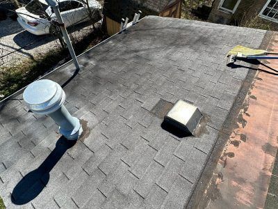 A roof with a vent on it and a car parked in the background.