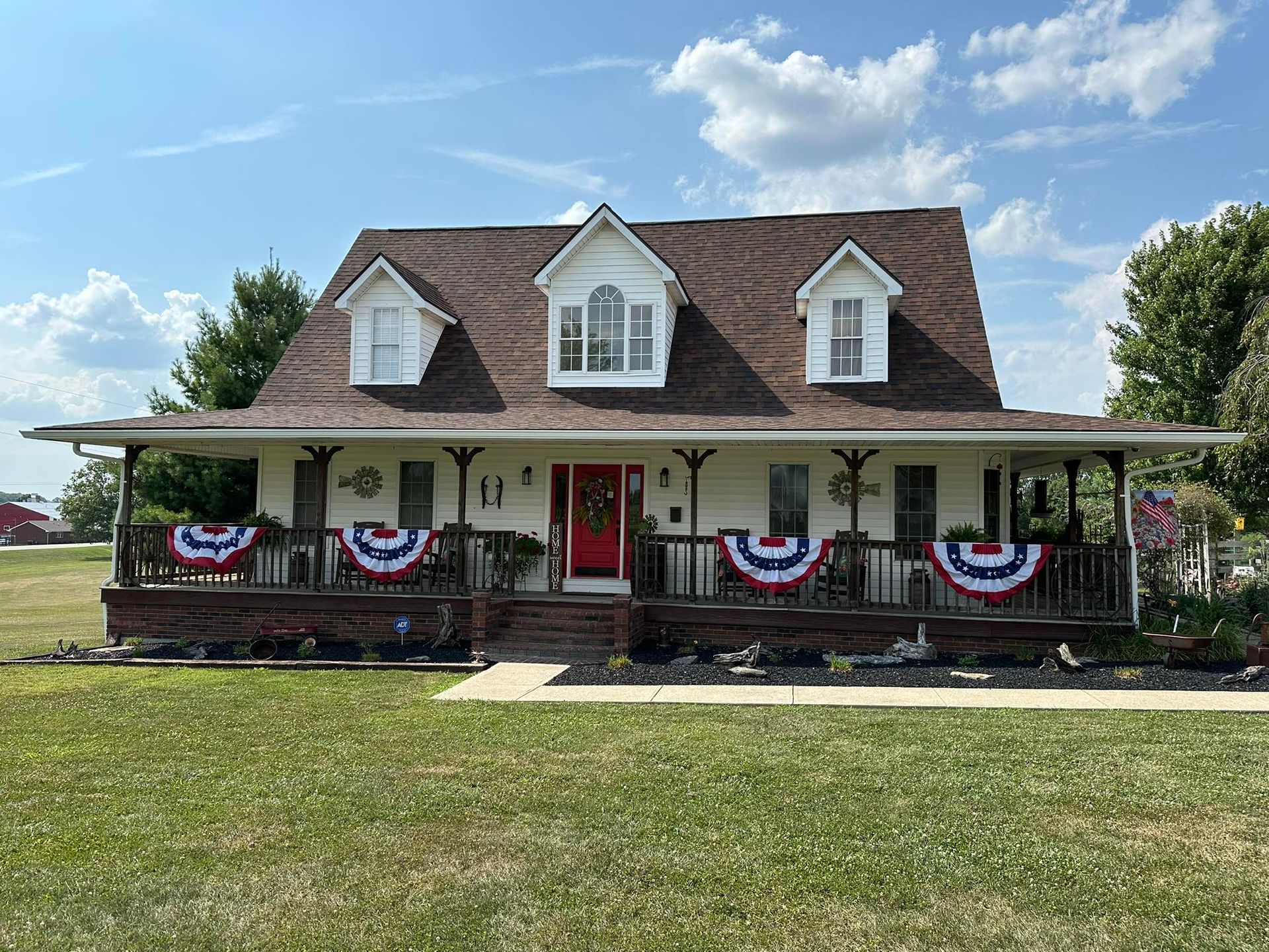 A large white house with a porch decorated with red , white and blue flags.