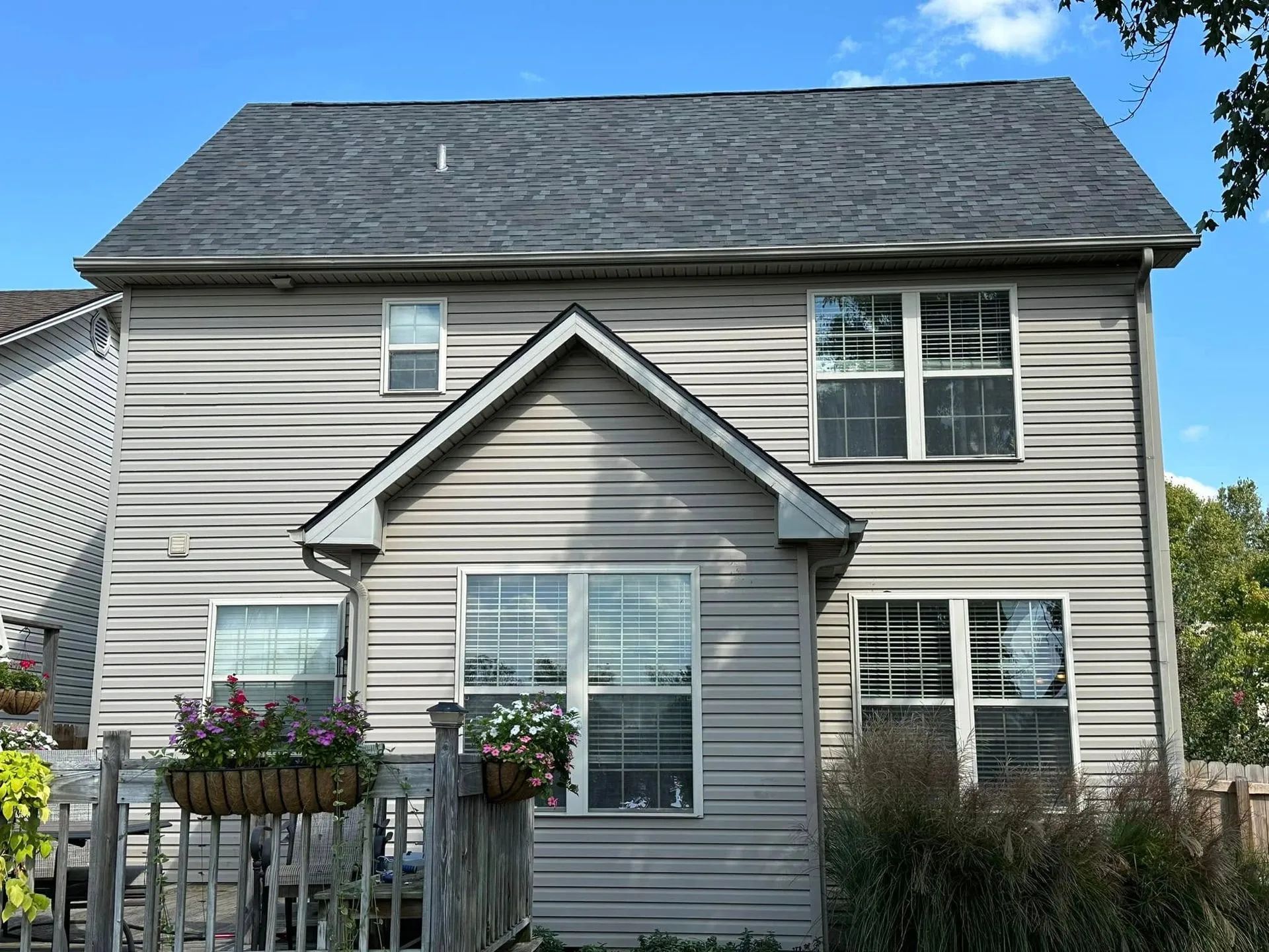 Rear view of a two-story house with gray siding, windows, and a dark gray roof against a blue sky.
