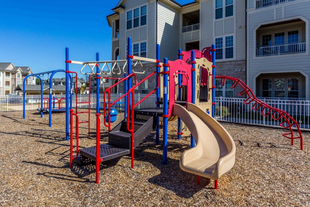 A playground with a slide, climbing wall, and swings in front of a building at Marquis Ellis Crossing in Durham, NC
