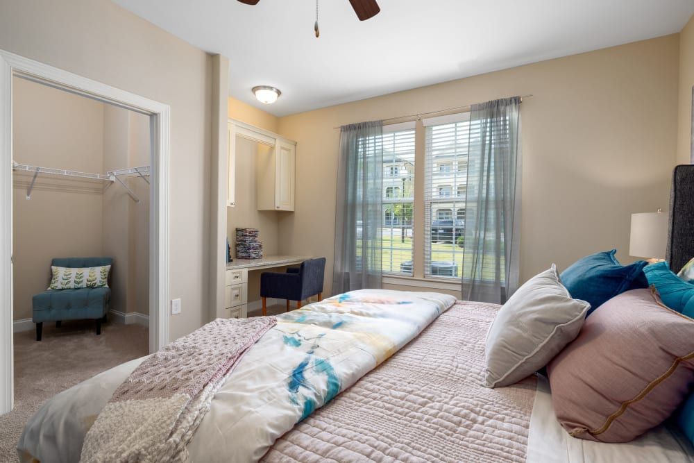 A bedroom with a large bed, desk, chair, and window at Marquis Ellis Crossing in Durham, NC.