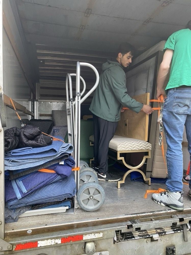 Two men loading furniture into a moving truck. One is securing a chair with a strap.