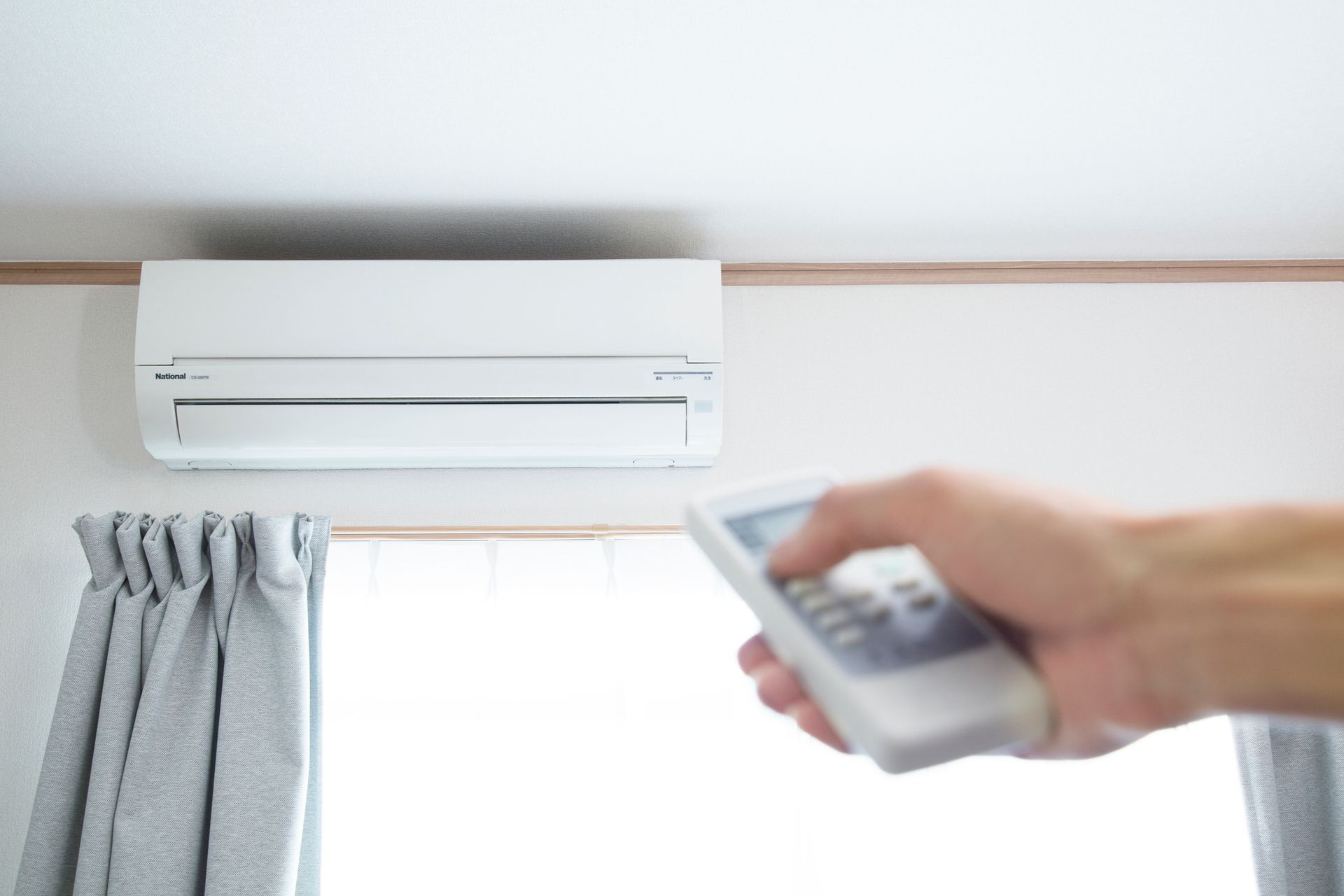 Homeowner using a remote control to operate a ductless mini split air conditioning system.