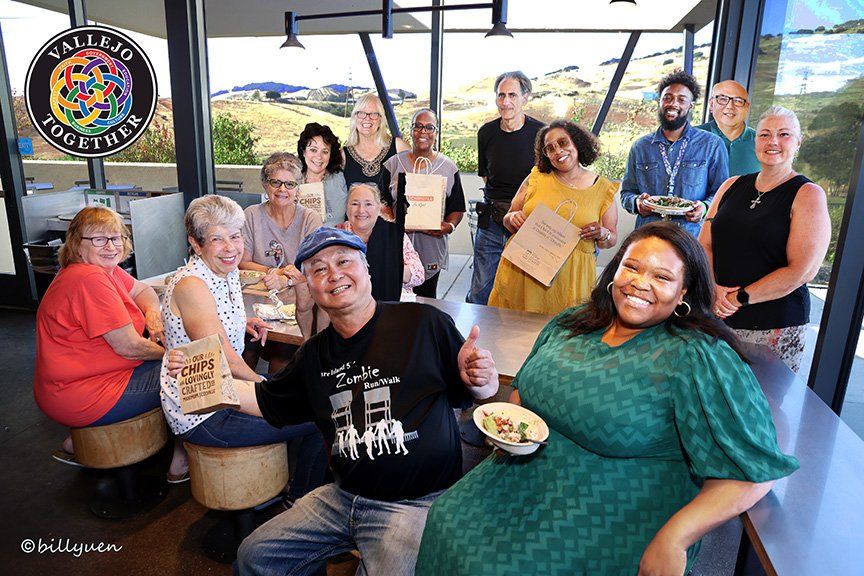 Group of people posing with food and signs in a cafe with a logo visible.