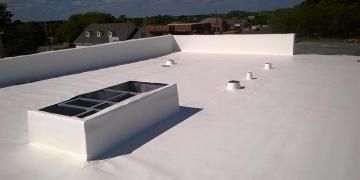 A flat, bright white roof surface with a rectangular skylight and several small ventilation pipes under a blue sky.