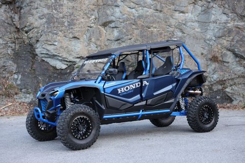 A blue atv is parked on the side of the road in front of a rock wall.