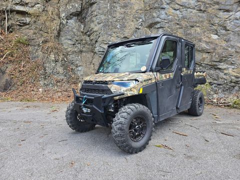 A polaris ranger 1000 is parked on the side of the road in front of a rock wall.