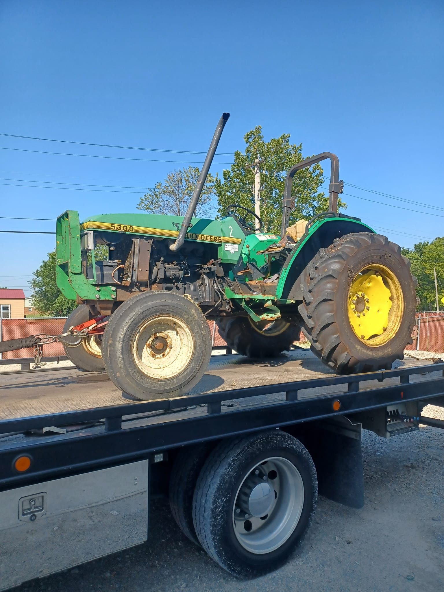 Green John Deere tractor on a flatbed tow truck against a blue sky.