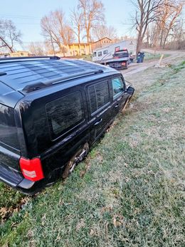 Black SUV stuck on grassy bank, tow truck in background.