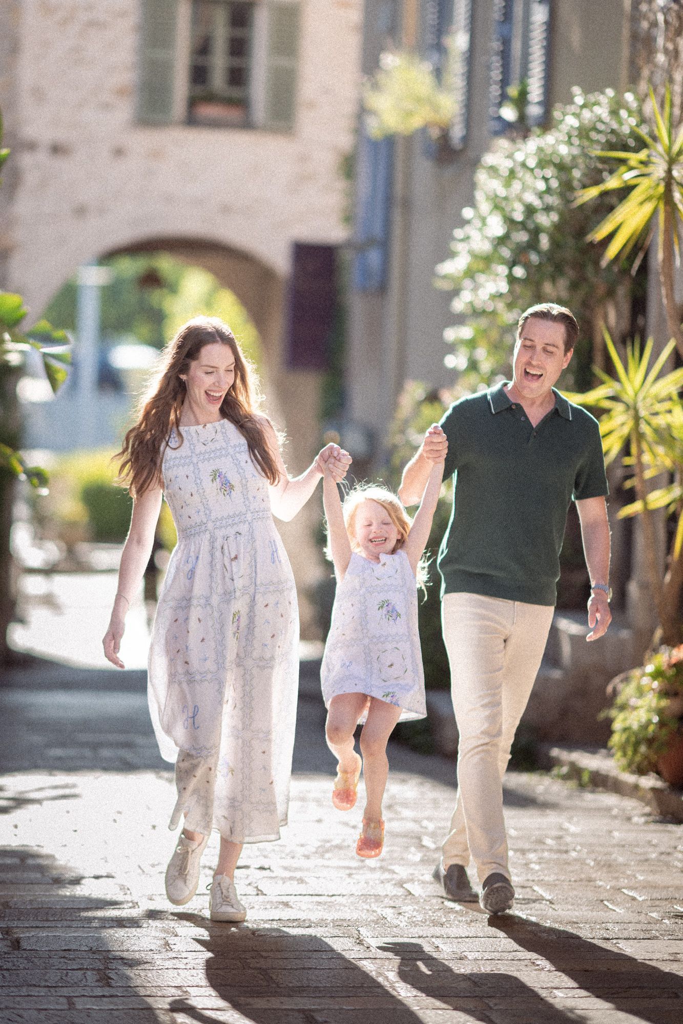 A mum and dad walking and laughing with their daughter on the streets on Valbonne, France, during a family photography session.