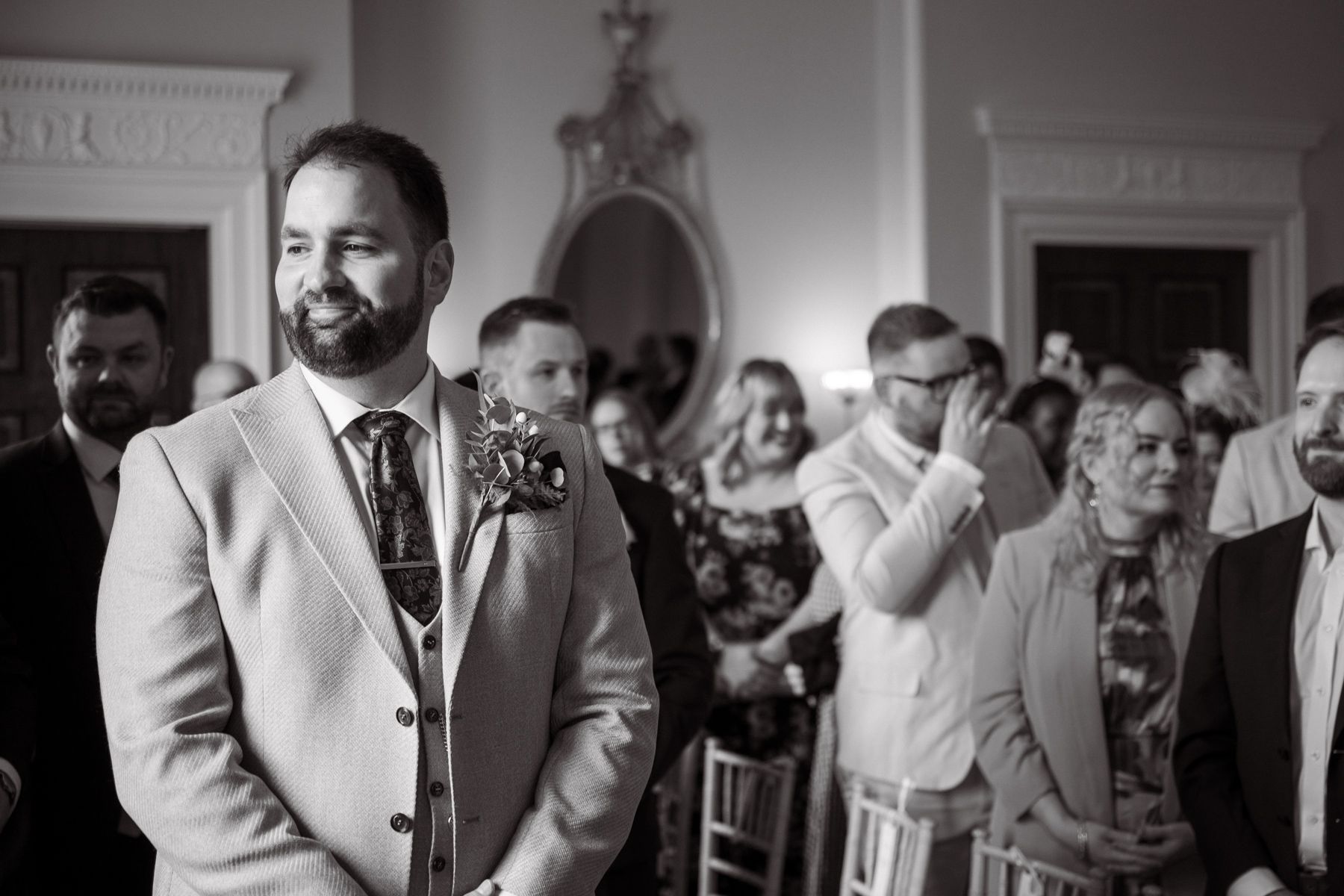 The groom waits for his bride, looking nervous, at the front of the aisle.