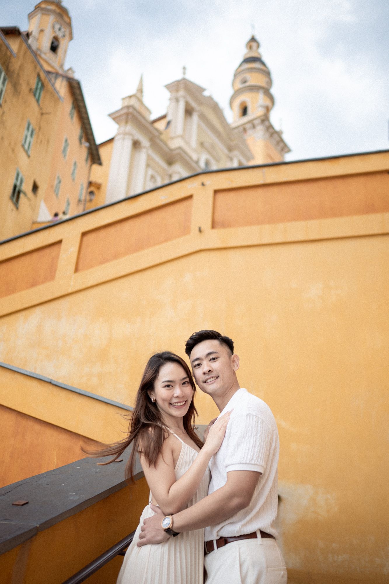 A couple laugh and smile on Menton's yellow stairs