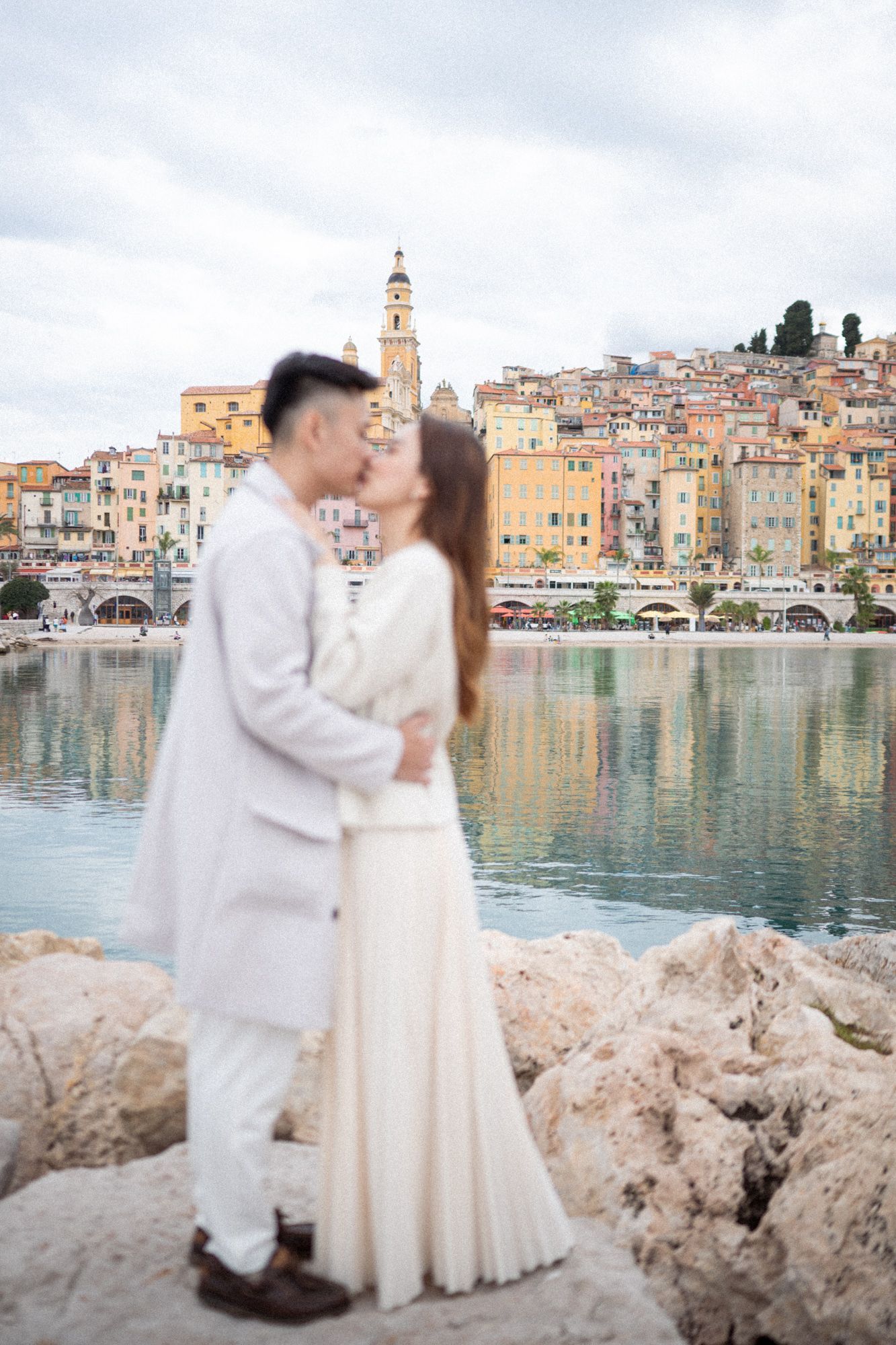A couple kissing behind the backdrop of Menton old town.