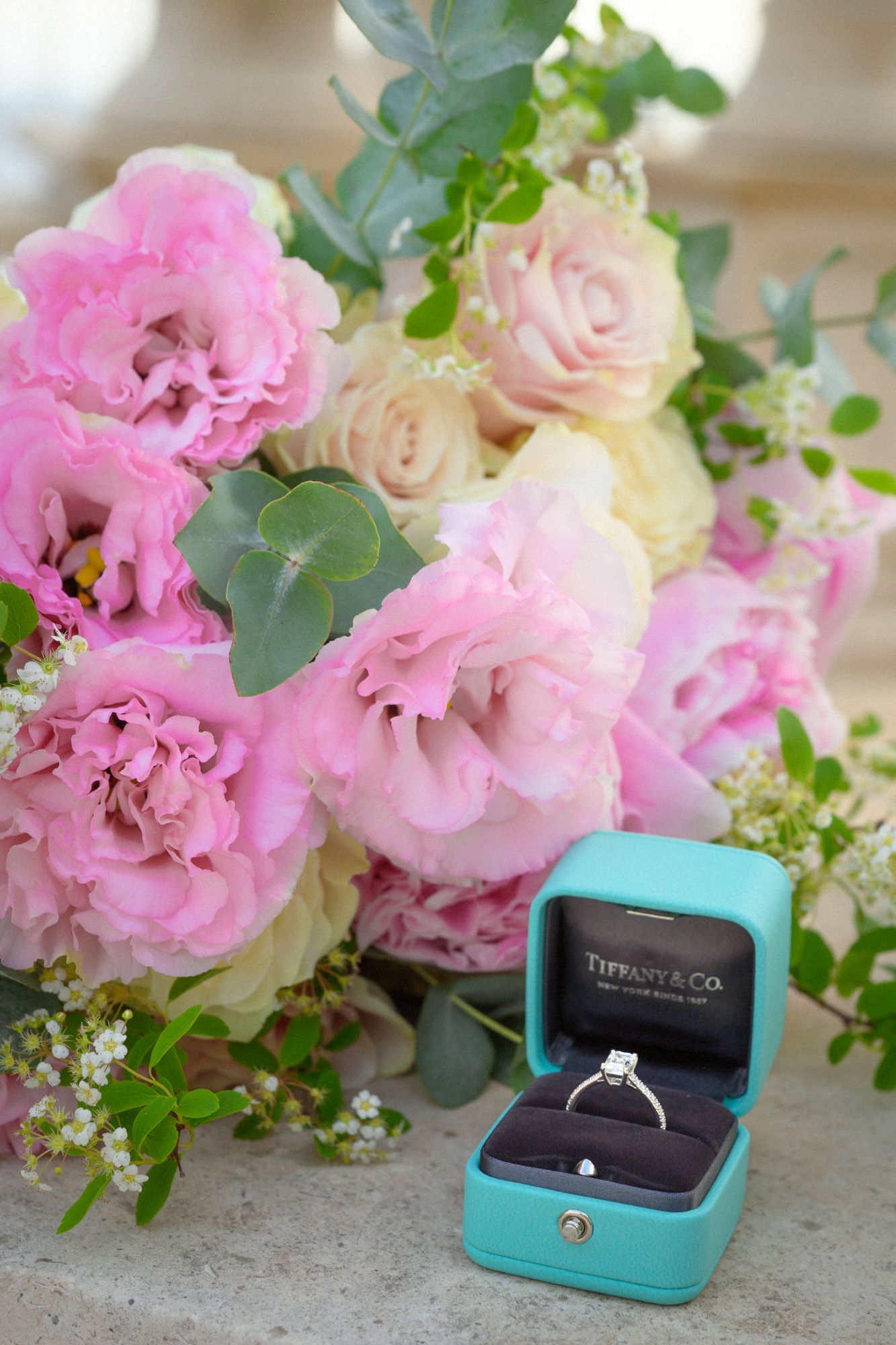A diamond ring next to a bouquet of flowers.