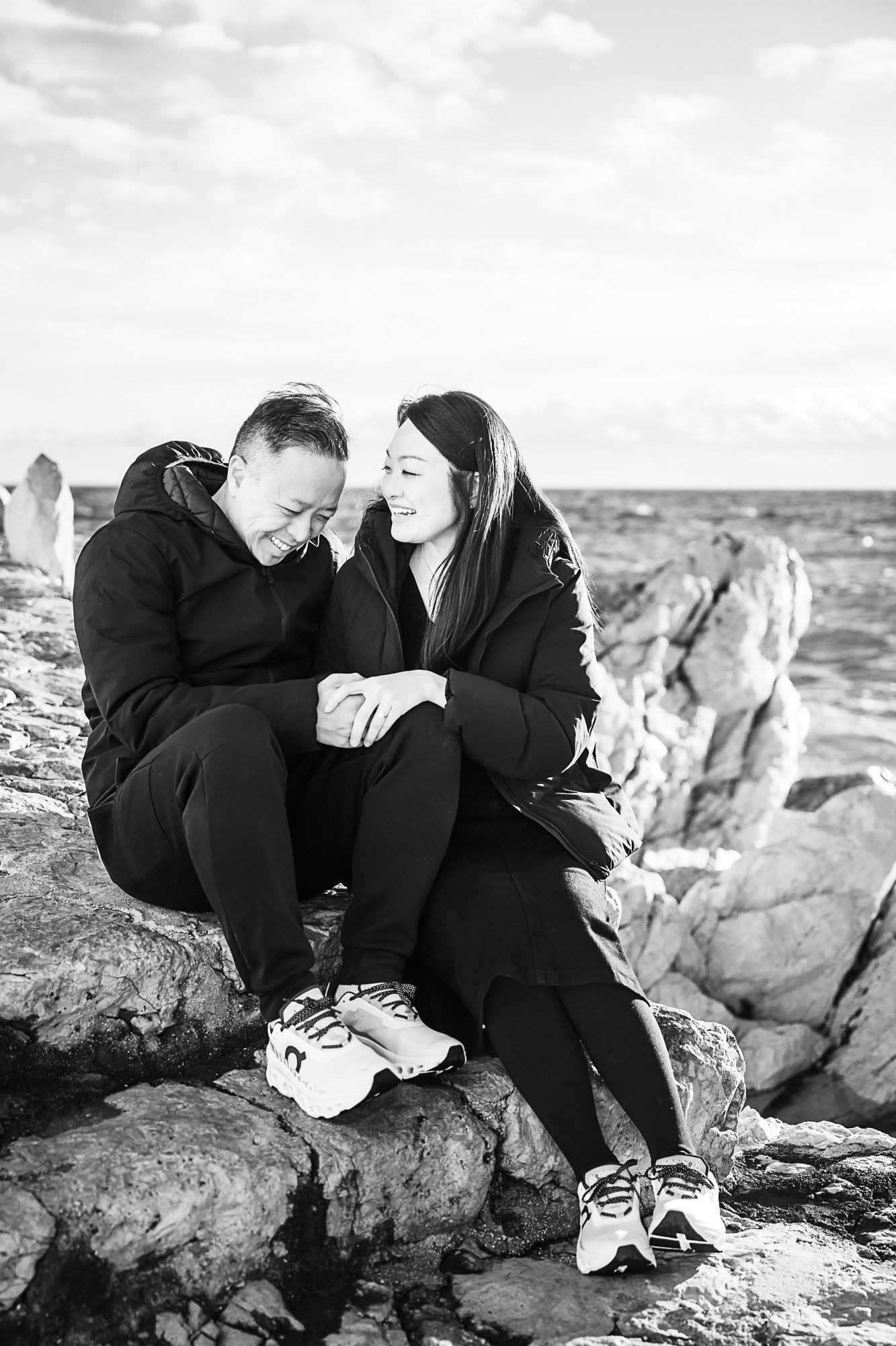 A couple laugh sitting on the rocks at Coco Beach, Nice, during a photoshoot