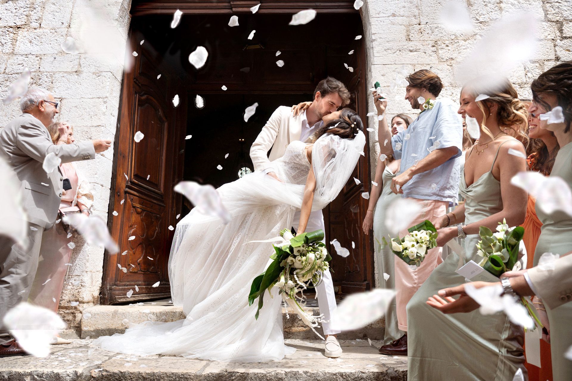 A groom kissing a bride under confetti outside a church in the south of France.