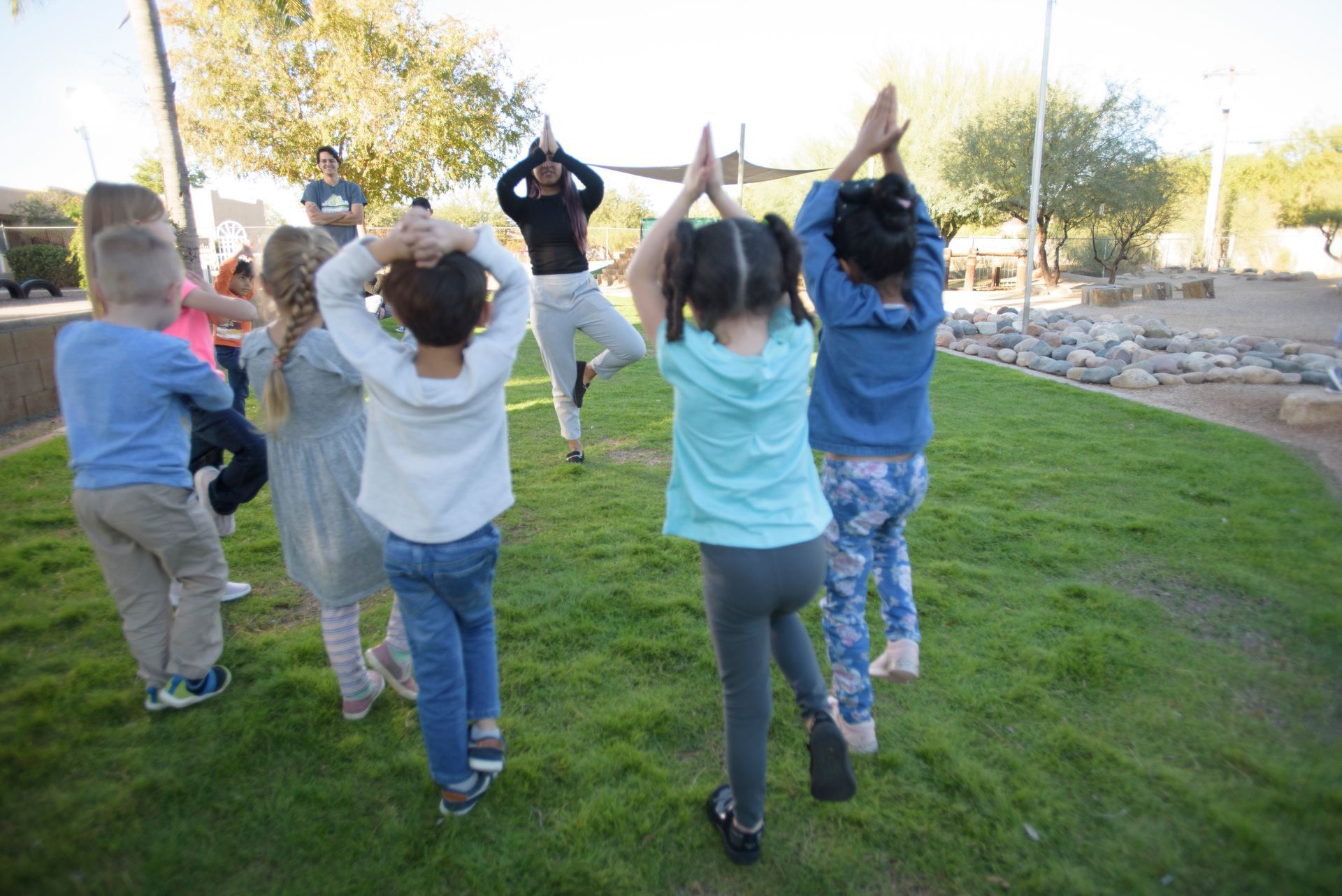 Children exercising outdoors on a grassy lawn, raising their arms together in a group workout