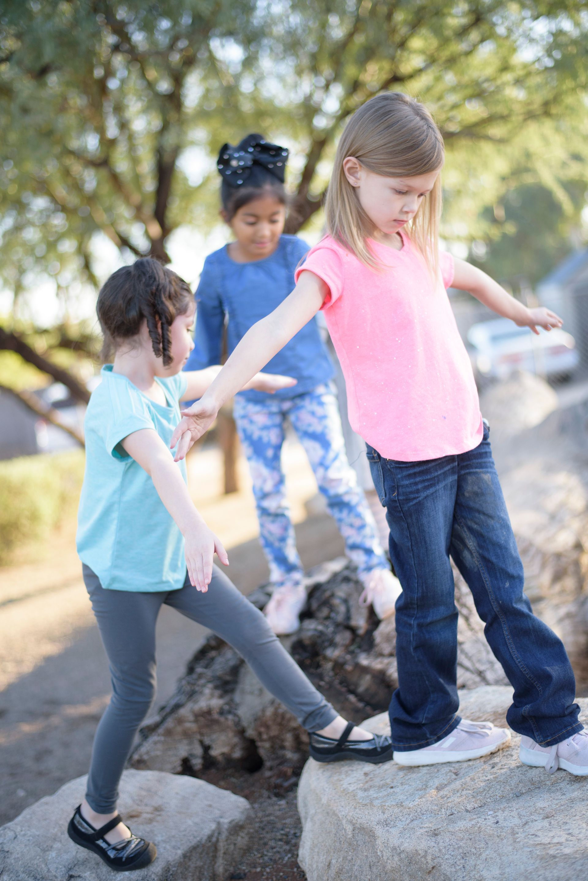 Three children balancing on large rocks outdoors in a sunny playground