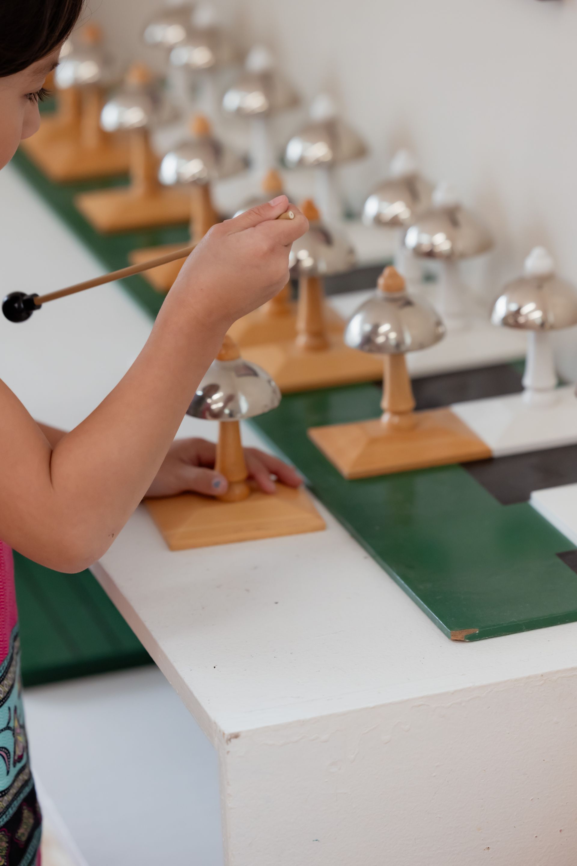 Person striking metal bells on a tabletop xylophone-like instrument in a music setting
