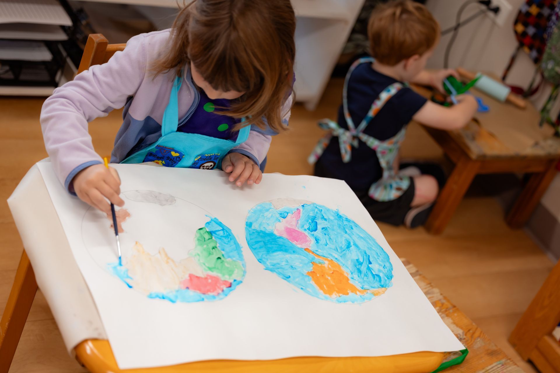 Children painting at a table with colorful paper fish artwork in a classroom