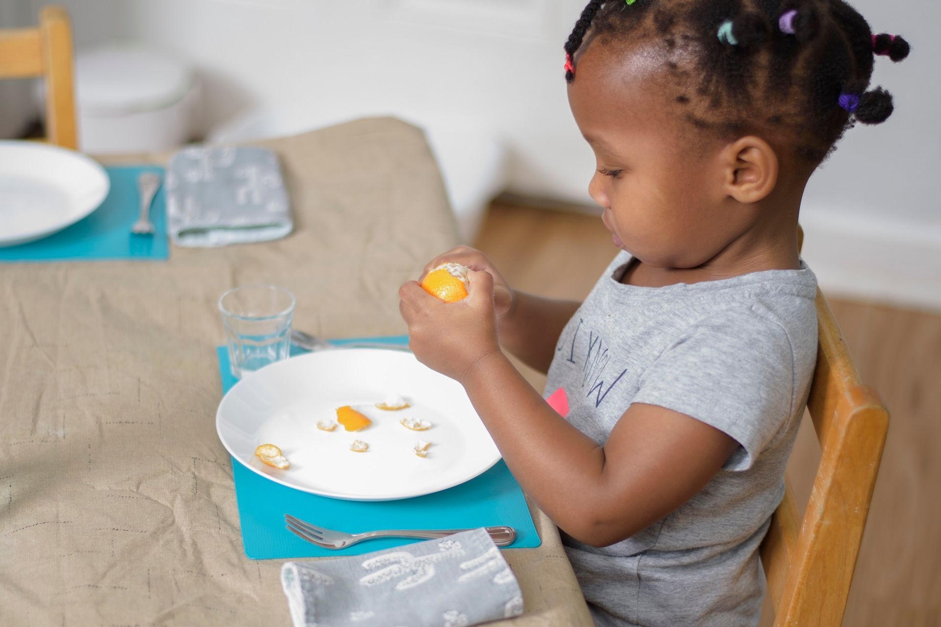 Young child opening a snack over a plate at a table with a blue lunch box