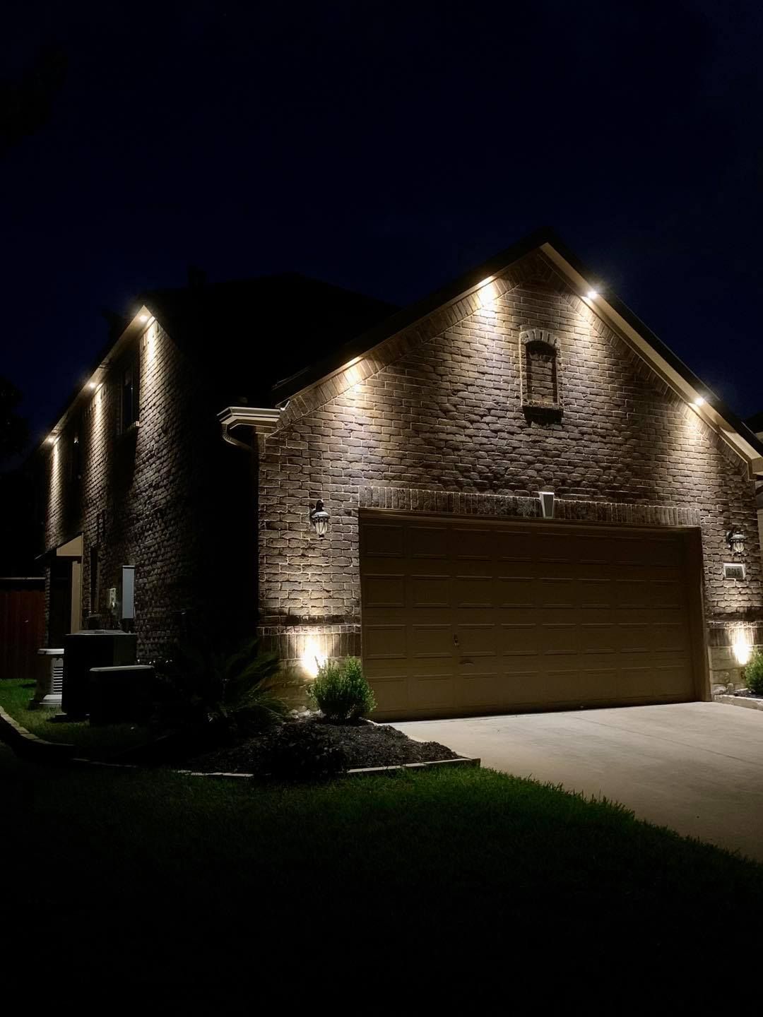 Brick house at night, lit by warm exterior lights, with a double garage and dark lawn.