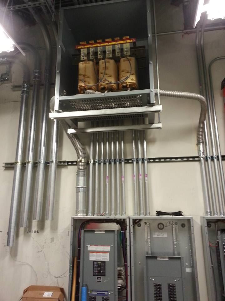 Electrical panels and conduit on a utility room wall, with a mounted transformer above.