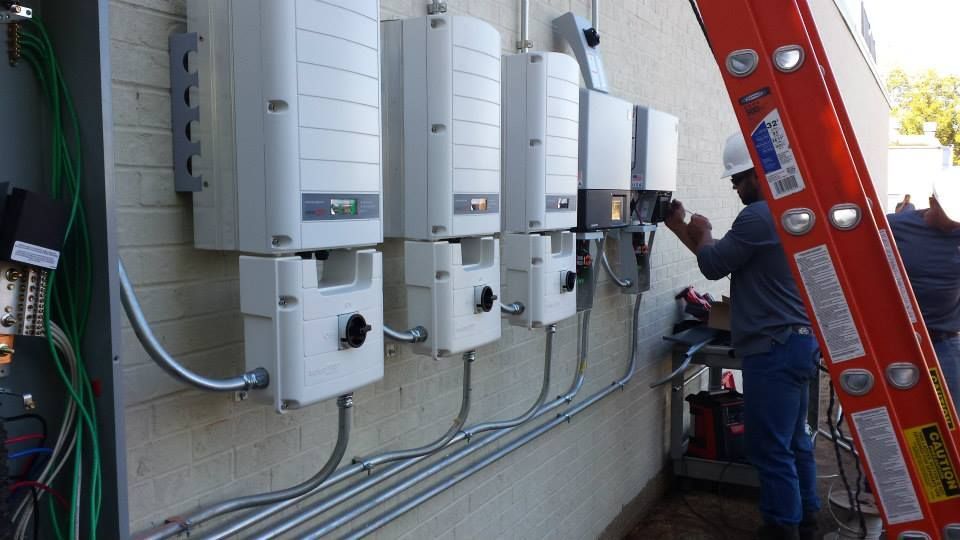 Technician working beside mounted electrical meters and red ladder against an exterior wall