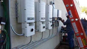 Technician working on wall-mounted electrical panels beside a red ladder outdoors